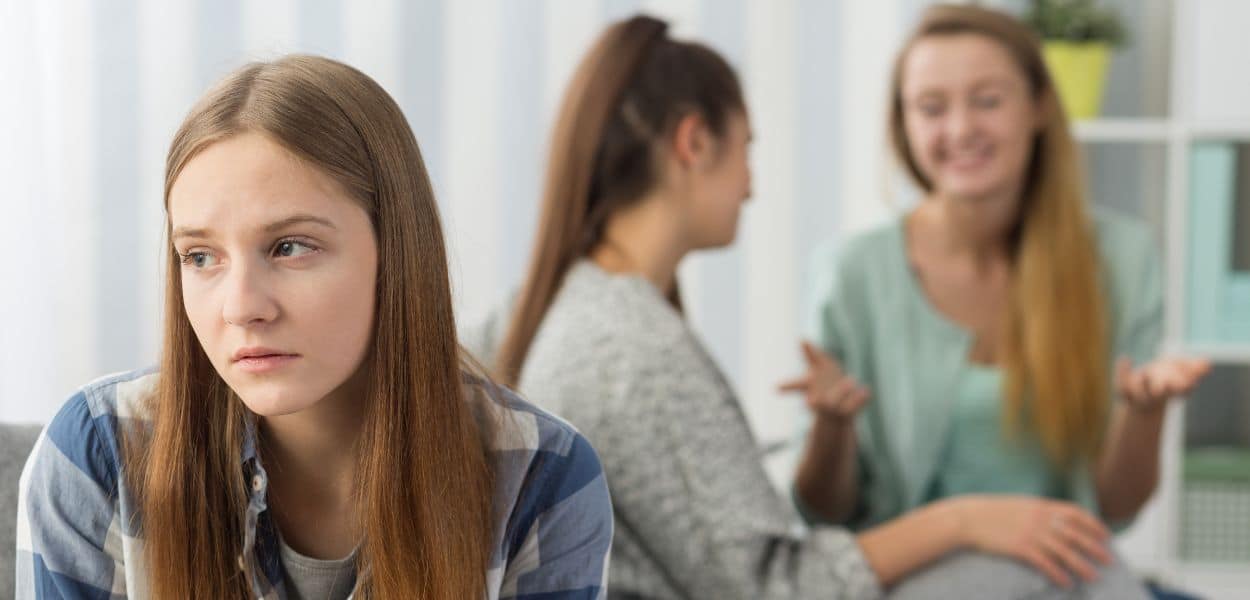 A group of girls talking on a couch with one girl being left out of the conversation.