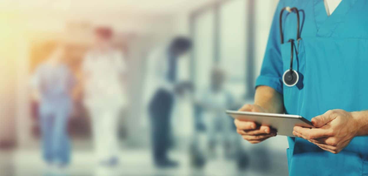 A healthcare professional holding a clipboard in a hospital hallway.