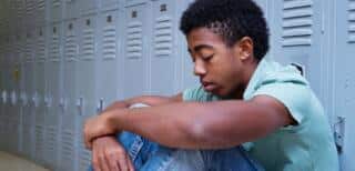 An African-American young adult sitting by a row of lockers.