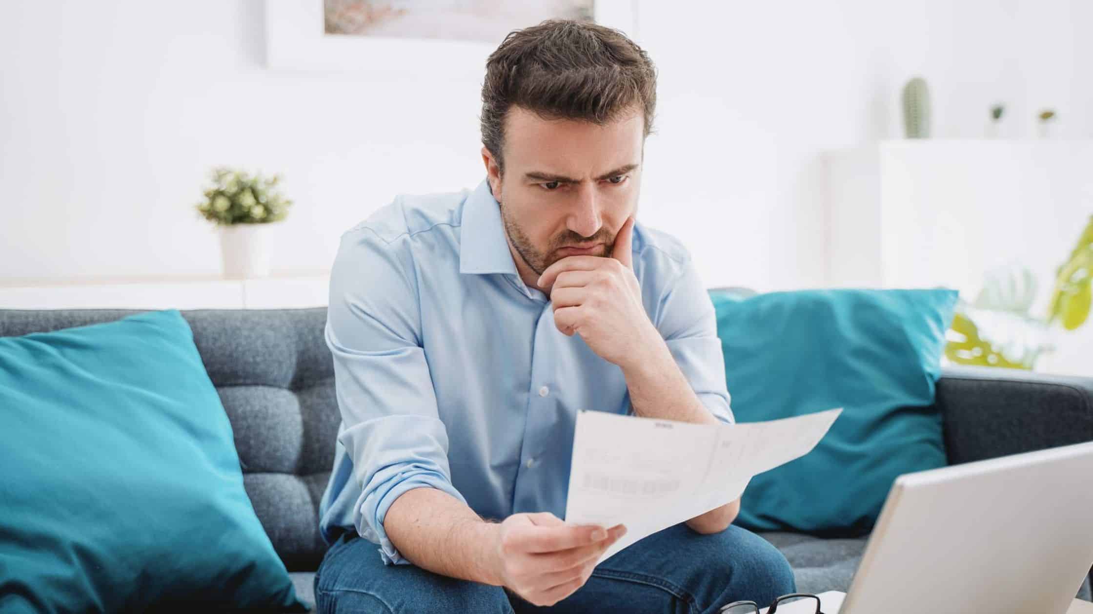 A man looking at paperwork, sitting on his couch.