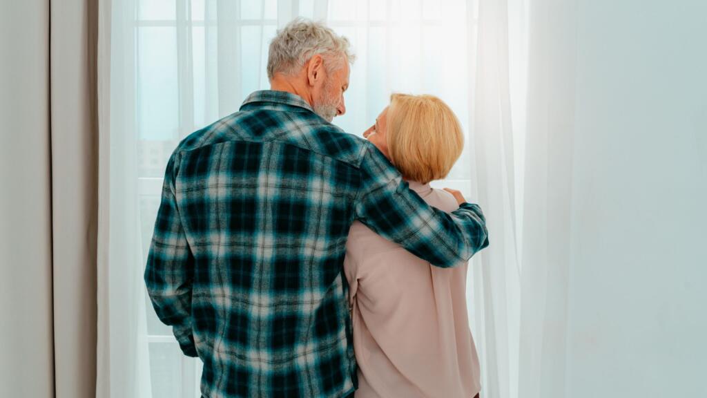 An older couple hugging and looking out the window.