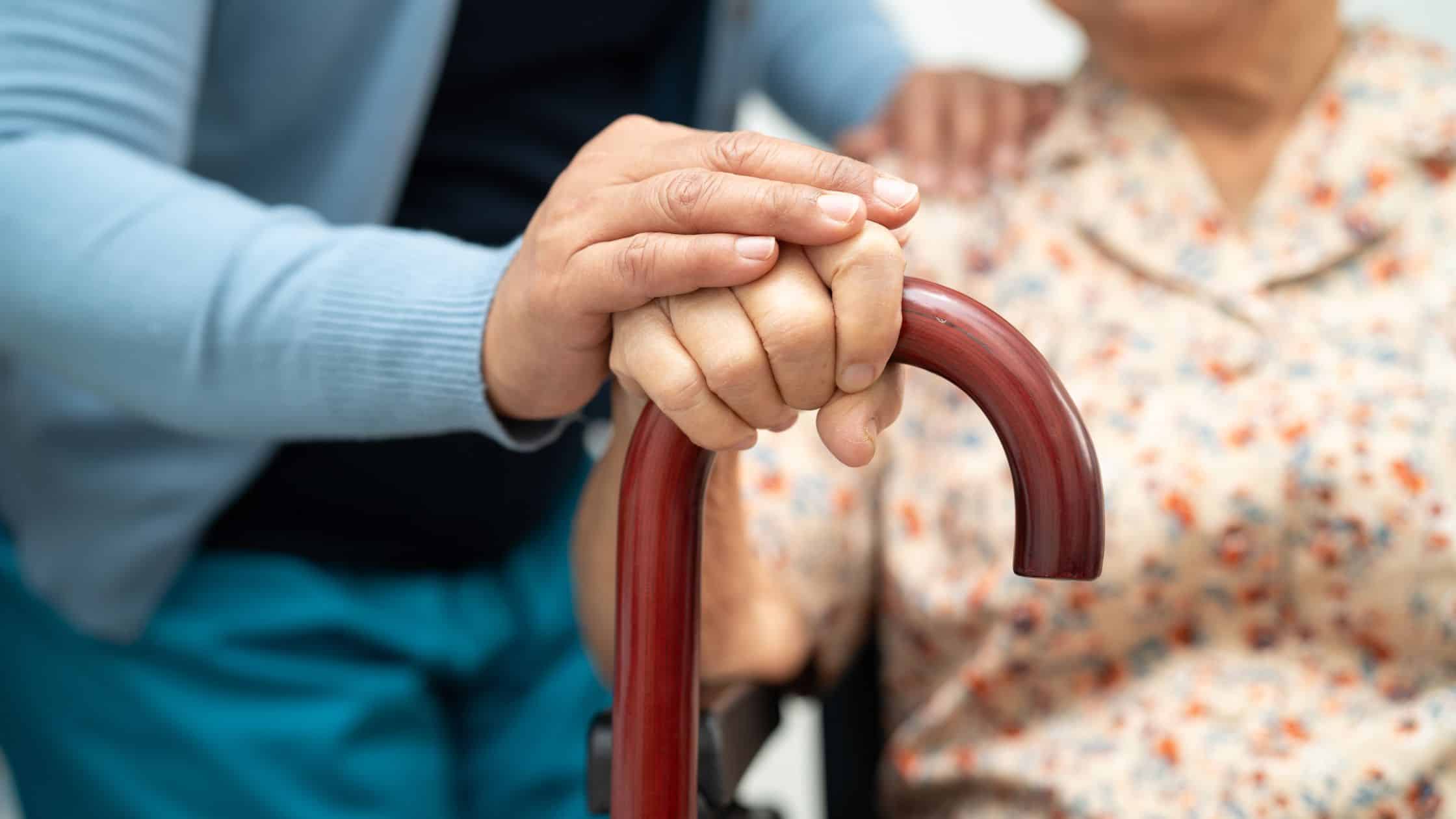 An elderly woman holding a cane, being reassured by a nurse.