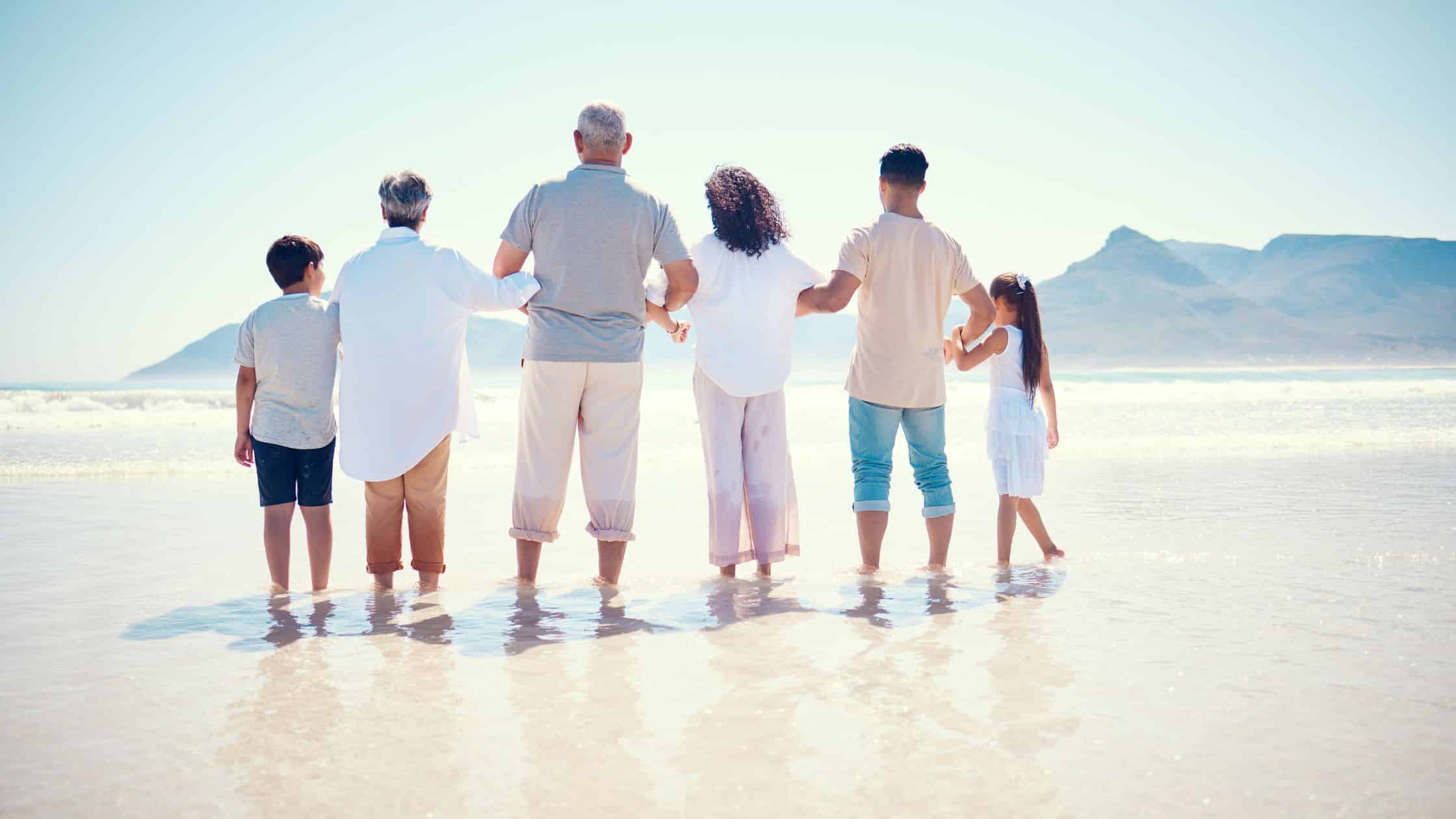 A multi-generational family standing together on a beach.