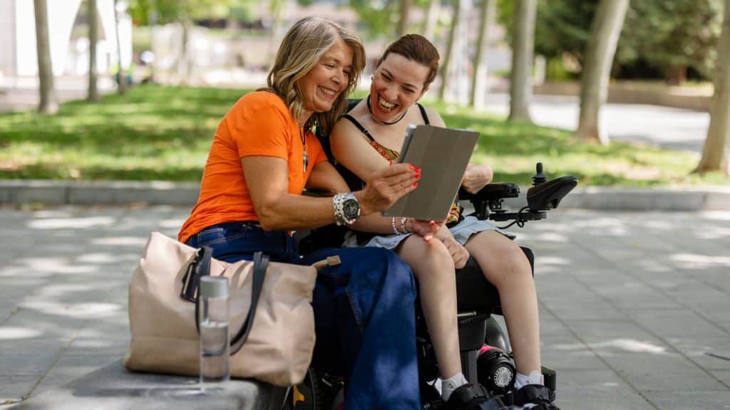 A young woman in a wheelchair and her mother looking at pictures on a tablet.